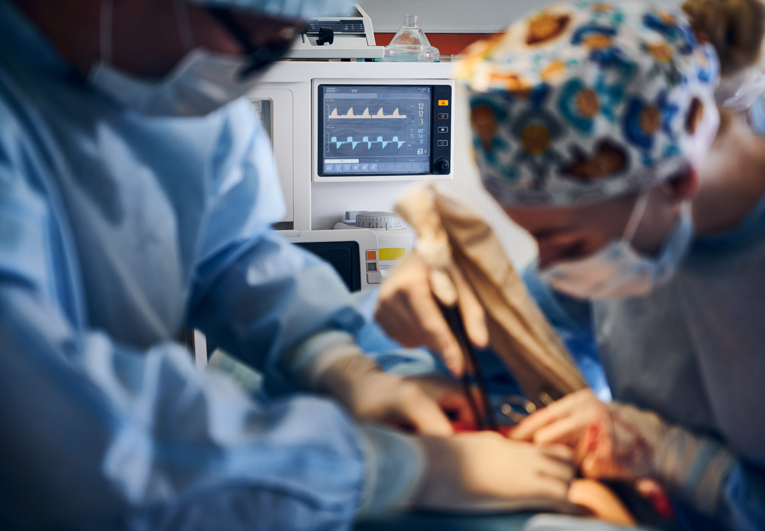 Focus on heart rate monitor and medical team performing tummy tuck surgery in operating room. Plastic surgeon and assistant removing excess fat from patient abdomen. Concept of abdominoplasty.